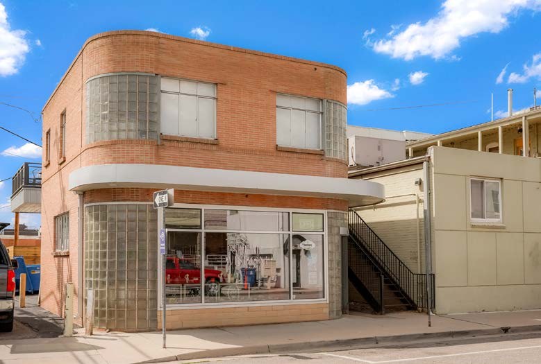 The two-storey brick building at 5711 S Nevada St, with a curved glass-block corner and a large shopfront window
