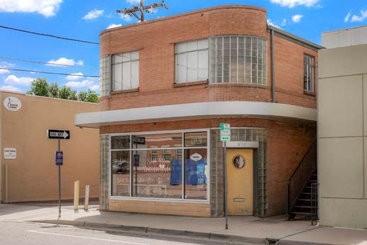 Front of the building from across Nevada Street, showing the shopfront window, round-windowed door and curved glass-block corners