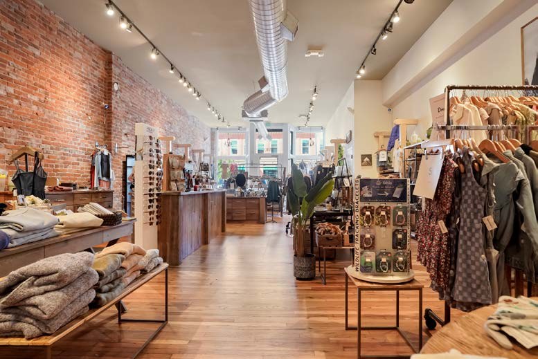 Inside Ruby Jane Boutique: clothing racks and display tables along an exposed brick wall